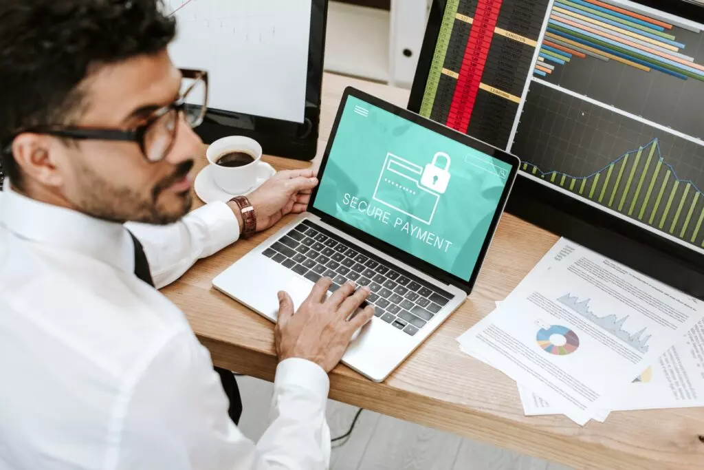 Mann mit Hemd und Brille vor Diagrammen und Laptop mit Fokus auf ‚Secure Payment